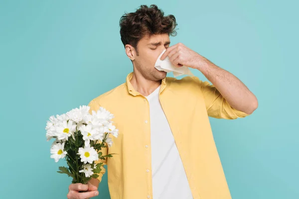 Uomo soffiando fuori naso con tovagliolo e tenendo bouquet con mano tesa isolato su blu — Foto stock