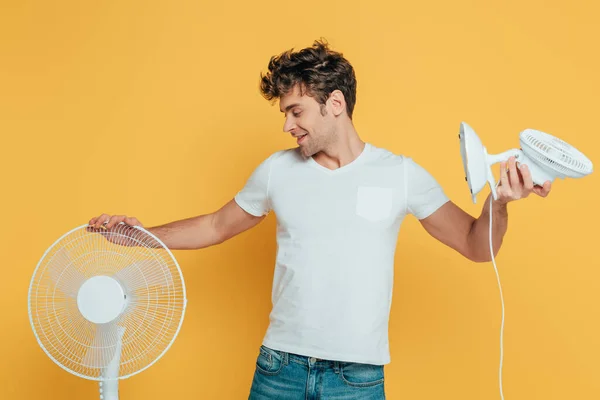 Hombre con ventiladores eléctricos y de escritorio sonriendo aislado en amarillo - foto de stock