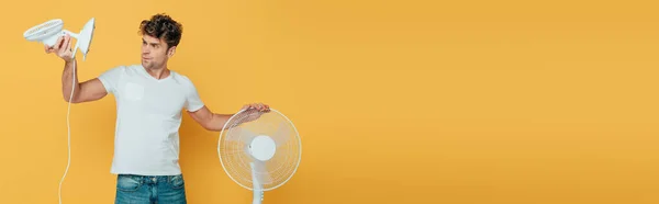 Concentrated and worried man looking at desk fan isolated on yellow, panoramic shot — Stock Photo