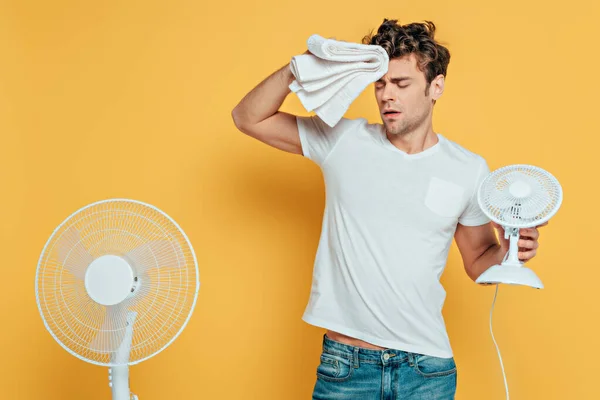Homme avec serviette, ventilateurs électriques et de bureau souffrant de chaleur sur jaune — Photo de stock