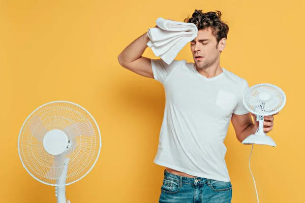 Mann mit Handtuch, Elektro- und Schreibtischventilatoren leidet unter Hitze auf gelb — Stockfoto