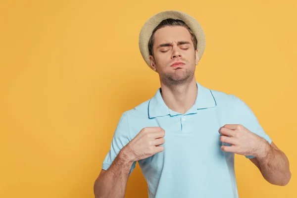 Homme aux yeux fermés souffrant de chaleur et T-shirt touchant isolé sur jaune — Photo de stock