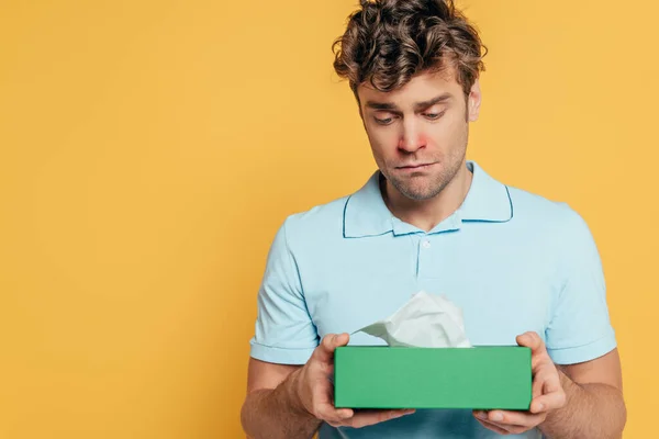 Sad and sick man holding box with napkins isolated on yellow — Stock Photo