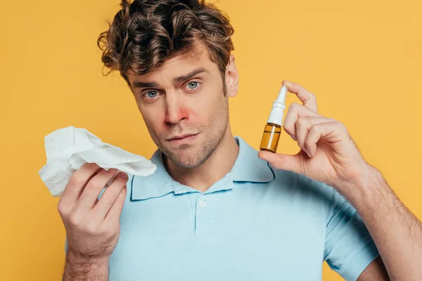 Portrait of sick man looking at camera and showing bottle of nasal drops and napkins isolated on yellow — Stock Photo