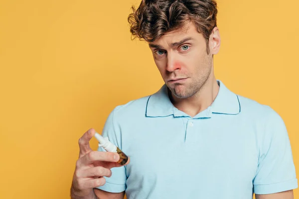 Hombre enfermo sosteniendo una botella de gotas nasales y mirando a la cámara aislada en amarillo - foto de stock