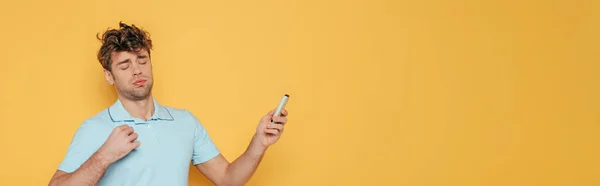 Homme avec télécommande à la main tendue souffrant de chaleur isolée sur plan jaune, panoramique — Photo de stock