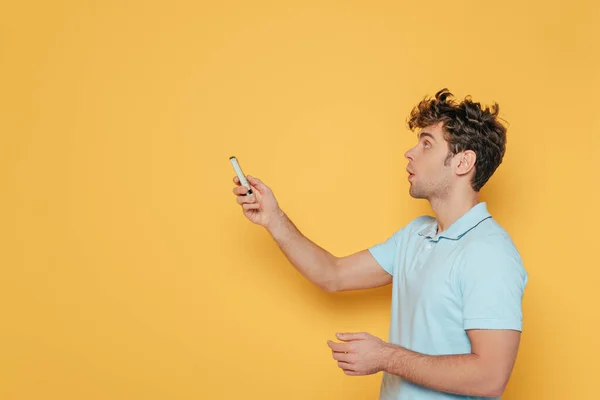 Homem segurando controlador remoto com a mão estendida no amarelo — Fotografia de Stock