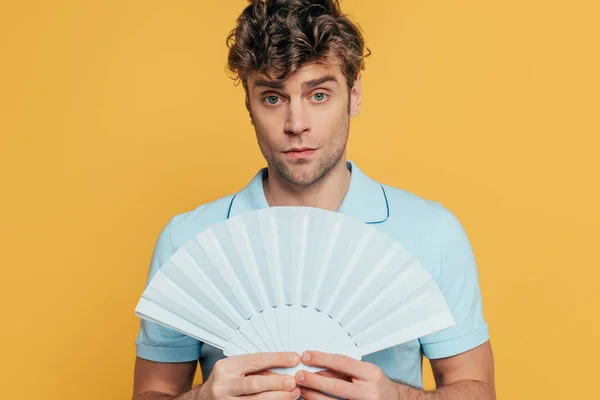 Homme tenant ventilateur main et regardant la caméra isolée sur jaune — Photo de stock