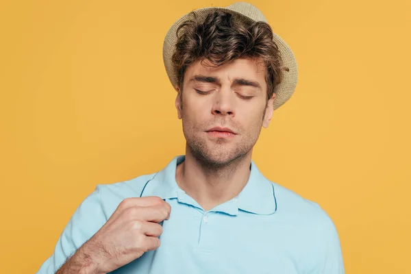 Homme au chapeau aux yeux fermés touchant T-shirt isolé sur jaune — Photo de stock