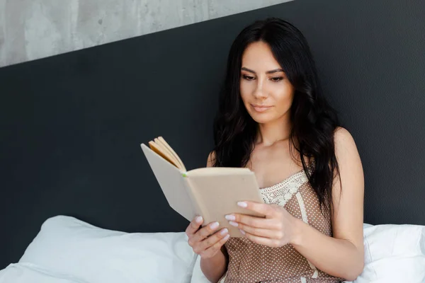 Belle jeune femme lecture livre sur lit à la maison — Photo de stock