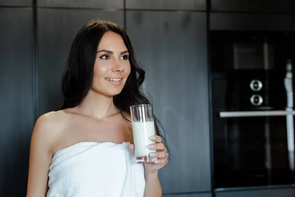 Позитивная женщина в полотенце держа стакан норки на кухне утром — стоковое фото