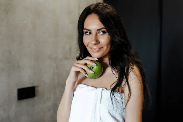 Beautiful woman in towel holding apple on kitchen in morning — Stock Photo