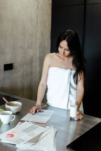 Bela mulher em toalha fazendo papelada durante o café da manhã na cozinha de manhã — Fotografia de Stock