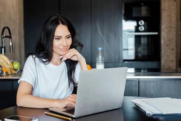Beautiful woman working with laptop and business documents on kitchen on self isolation — Stock Photo