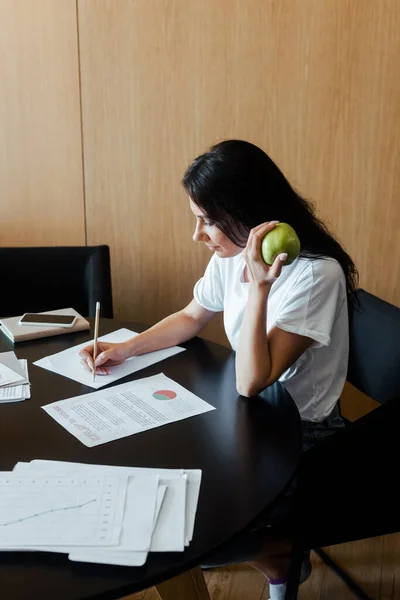 Frau arbeitet mit Geschäftsdokumenten und hält Apfel zu Hause in der Isolation — Stockfoto