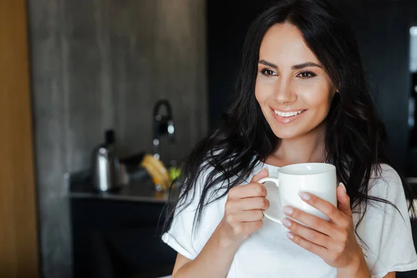 Красивая улыбающаяся молодая женщина держит чашку кофе дома — стоковое фото