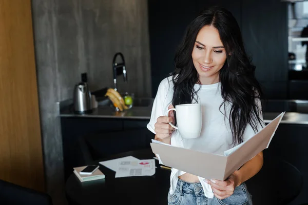 Молода жінка з чашкою кави, що працює з бізнес-документами вдома на самоізоляції — стокове фото
