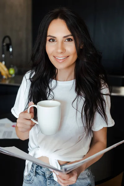 Mulher sorrindo com xícara de café trabalhando com documentos de negócios em casa em auto-isolamento — Fotografia de Stock