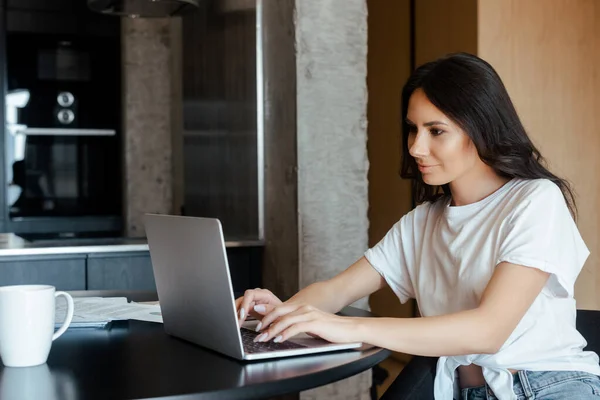 Beautiful woman working on laptop with business documents on kitchen on self isolation — Stock Photo