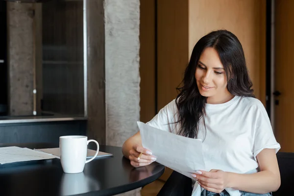 Красивая женщина, работающая с деловыми документами и чашкой кофе дома на самоизоляции — стоковое фото