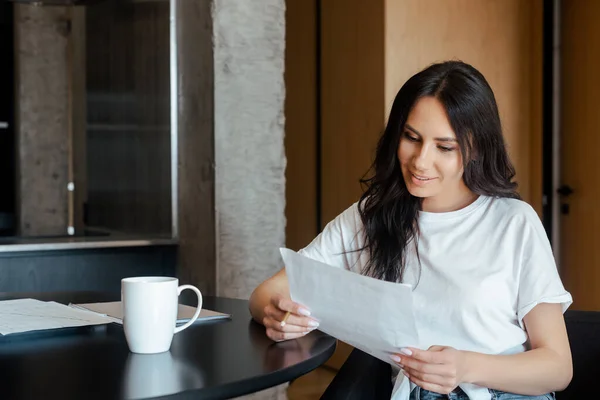 Hermosa mujer que trabaja con documentos de negocios y taza de café en casa en auto aislamiento - foto de stock