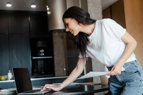 Mulher atraente que trabalha com laptop e documentos de negócios na cozinha em auto-isolamento — Fotografia de Stock