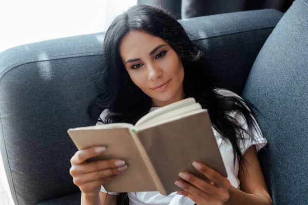 Felice donna lettura libro sul divano a casa — Foto stock