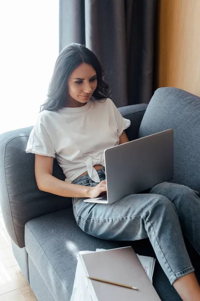 Красива жінка працює на ноутбуці з діловими документами на дивані — стокове фото