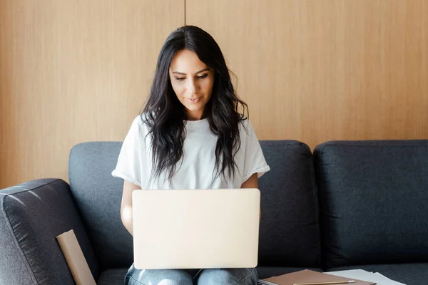 Красива молода жінка працює на ноутбуці з діловими документами на дивані — стокове фото