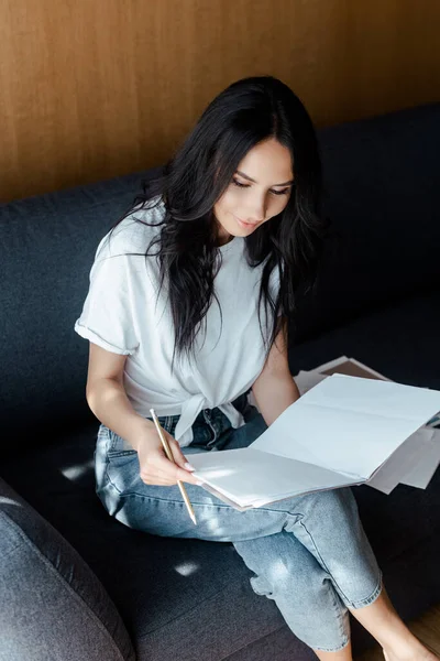 Красива молода жінка, що працює з діловими документами на дивані під час самоізоляції — стокове фото