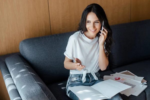 Glückliche Frau, die auf dem Smartphone spricht und während der Isolation mit Geschäftsdokumenten auf dem Sofa arbeitet — Stockfoto