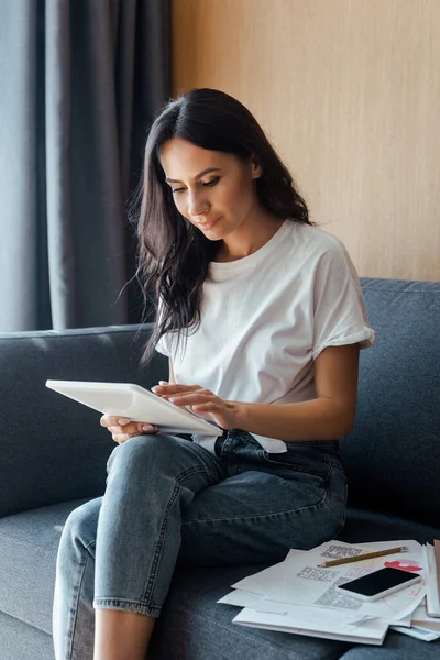 Schöne Frau arbeitet mit digitalem Tablet, Smartphone und Geschäftsdokumenten auf dem Sofa während der Selbstisolierung — Stockfoto