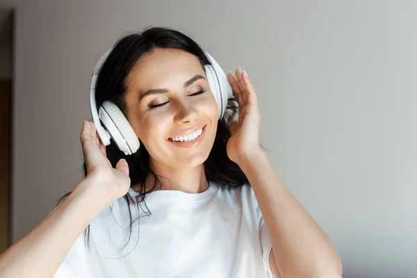 Fröhliche junge Frau mit geschlossenen Augen, die zu Hause mit Kopfhörern Musik hört — Stockfoto