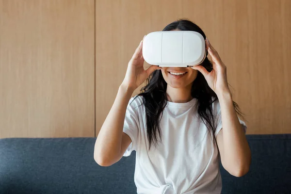 Mujer joven sonriente usando auriculares de realidad virtual en casa - foto de stock