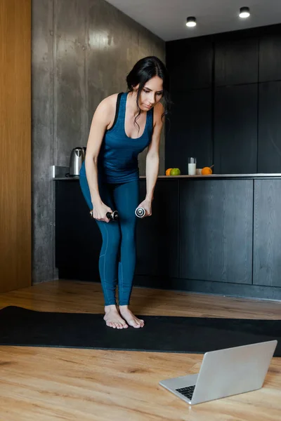 Mujer atlética con pesas en el entrenamiento de la estera de fitness en línea con el ordenador portátil - foto de stock