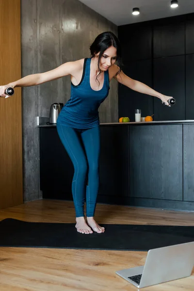 Glückliche athletische Frau mit Kurzhanteln auf Fitnessmattentraining online mit Laptop — Stockfoto