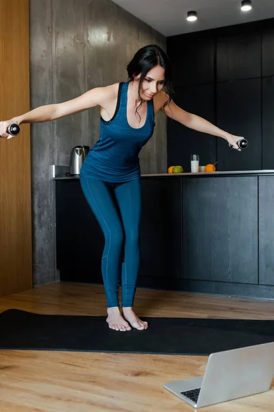 Mujer atlética feliz con pesas en el entrenamiento de la estera de fitness en línea con el ordenador portátil - foto de stock