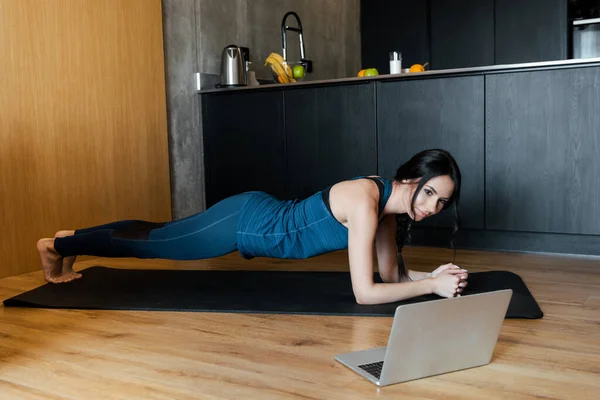 Спортивная женщина в доске на фитнес-коврик обучение онлайн с ноутбуком — стоковое фото