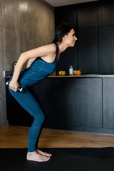 Glückliche athletische Frau hockt mit Hanteln auf Fitnessmatte — Stockfoto