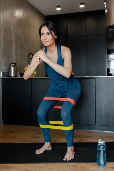 Спортивная женская тренировка с полосами сопротивления на коврике для фитнеса со спортивной бутылкой — стоковое фото