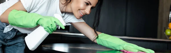 Heureuse fille en latex gants table de nettoyage avec chiffon et bouteille de pulvérisation, culture horizontale — Photo de stock