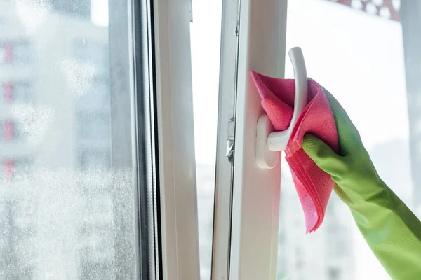 Ausgeschnittene Ansicht einer Frau in Gummihandschuhen, die Fenstergriff mit rosa Lappen putzt — Stockfoto