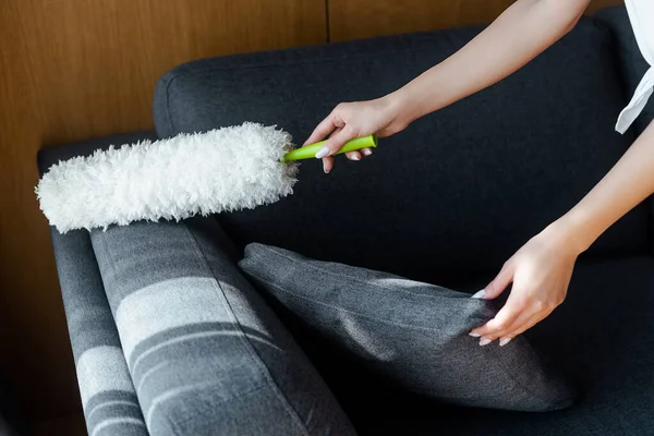 Vista recortada de la mujer limpiando el polvo del sofá con el plumero - foto de stock