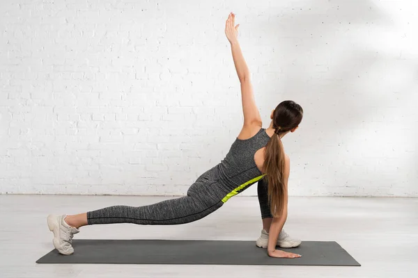 Vista posterior de la chica deportiva con la mano extendida haciendo ejercicio en la estera de fitness - foto de stock