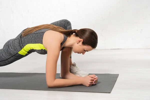 Profile of sportive young woman warming up on fitness mat — Stock Photo