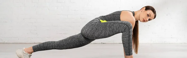 Panoramic shot of young and attractive sportswoman stretching and looking at camera — Stock Photo