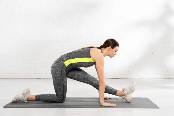 Side view of young sportswoman stretching on fitness mat — Stock Photo