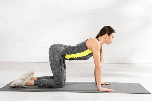 Profil de la jeune femme debout sur les genoux sur tapis de fitness — Photo de stock