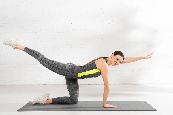 Mujer joven y feliz con la mano extendida haciendo ejercicio en la alfombra de fitness - foto de stock