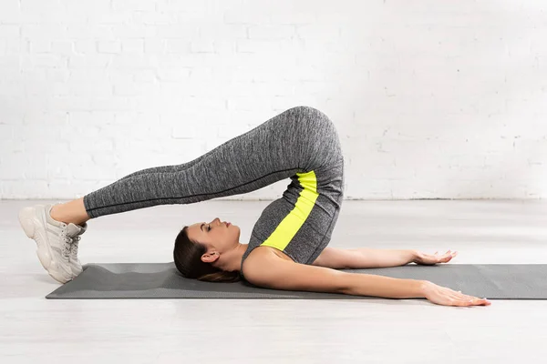 Vista lateral de la hermosa y flexible deportista haciendo ejercicio en la alfombra de fitness - foto de stock